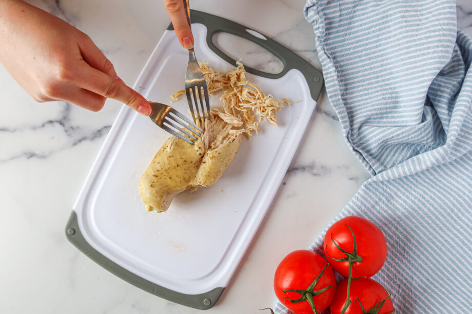 Two hand, a fork in each. One fork is holding the chicken breast in place, the other is pulling meat away from the breast. 