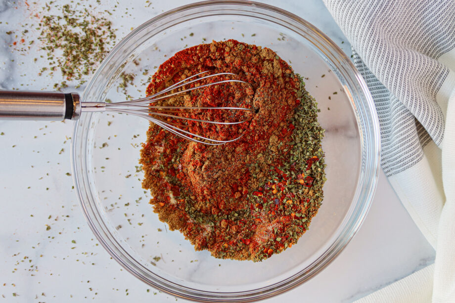 Homemade taco seasoning mix being whisked together in a glass bowl.