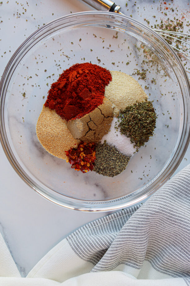 Spices for homemade taco seasoning measured into a glass mixing bowl. 