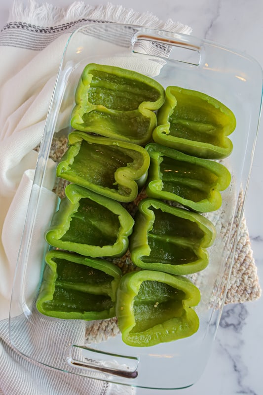 Green bell pepper halves in a glass baking dish.