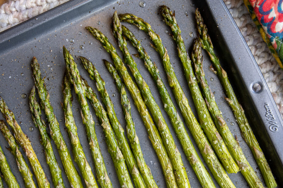 Close up of simple oven roasted asparagus on a dark grey baking sheet, baked and ready to eat!