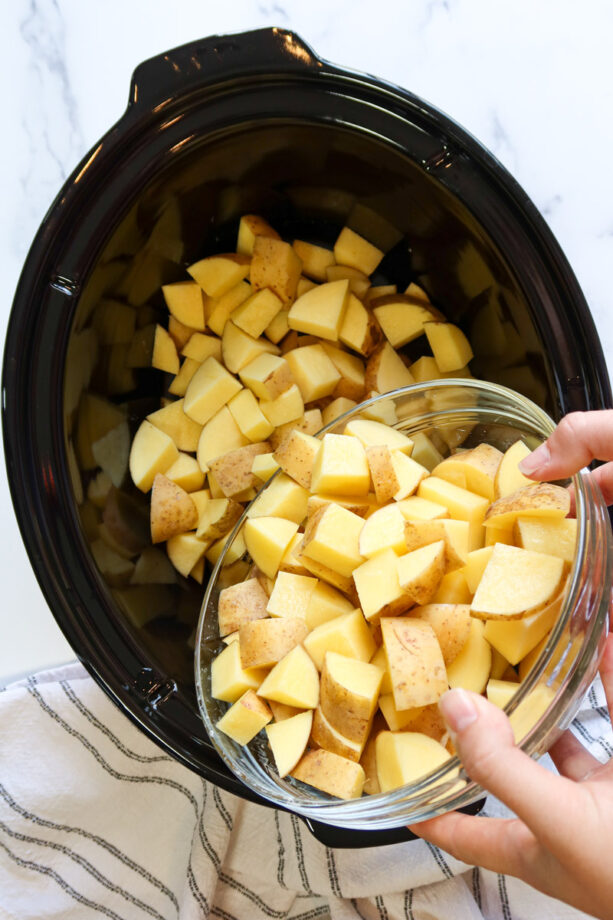 Transferring cubed potatoes from a glass bowl to a large, black crockpot.