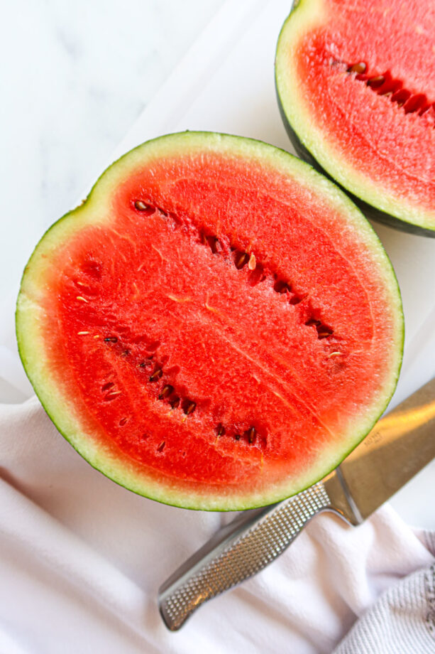 A watermelon cut in half. A silver knife sits to the side.