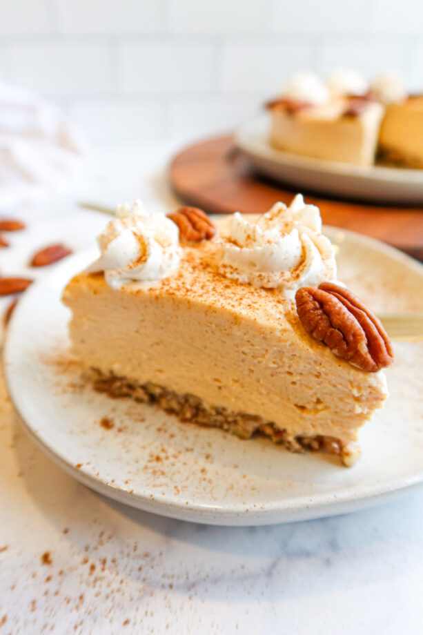 Close up of a slice of low carb, no-bake pumpkin cheesecake decorated with whip cream, pecans and sprinkled cinnamon. 