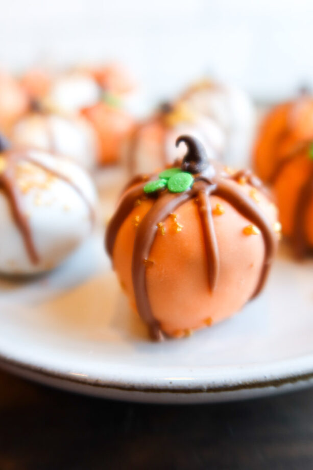 Close up of peanut butter chocolate chip bites on a small, white plate. Bites are decorated like tiny orange and white pumpkins!