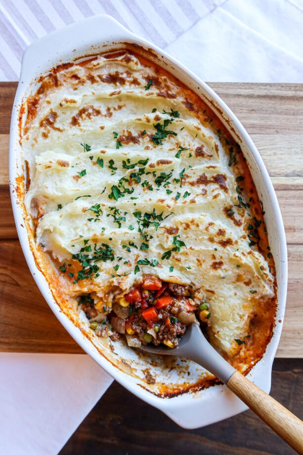 Homemade shepherd's pie in a white, porcelain baking dish with a wooden serving spoon.