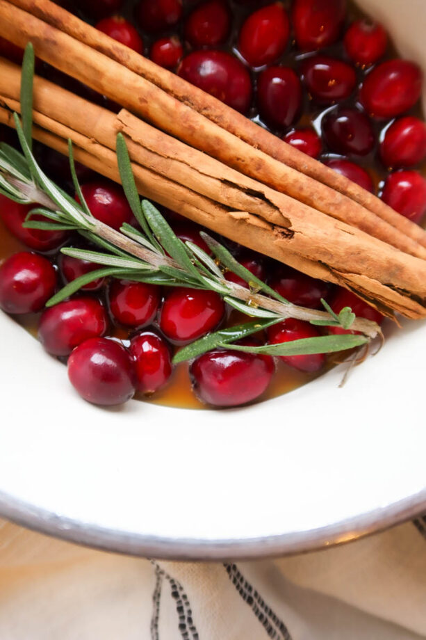 Cranberries, cinnamon sticks, fresh sprig of rosemary and maple syrup in a sauce pan.