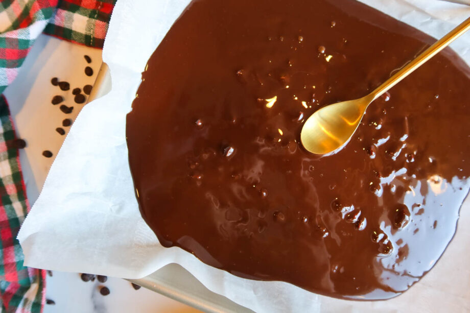 Melted chocolate mixed with crushed candy canes spread on a parchment paper lined baking sheet.