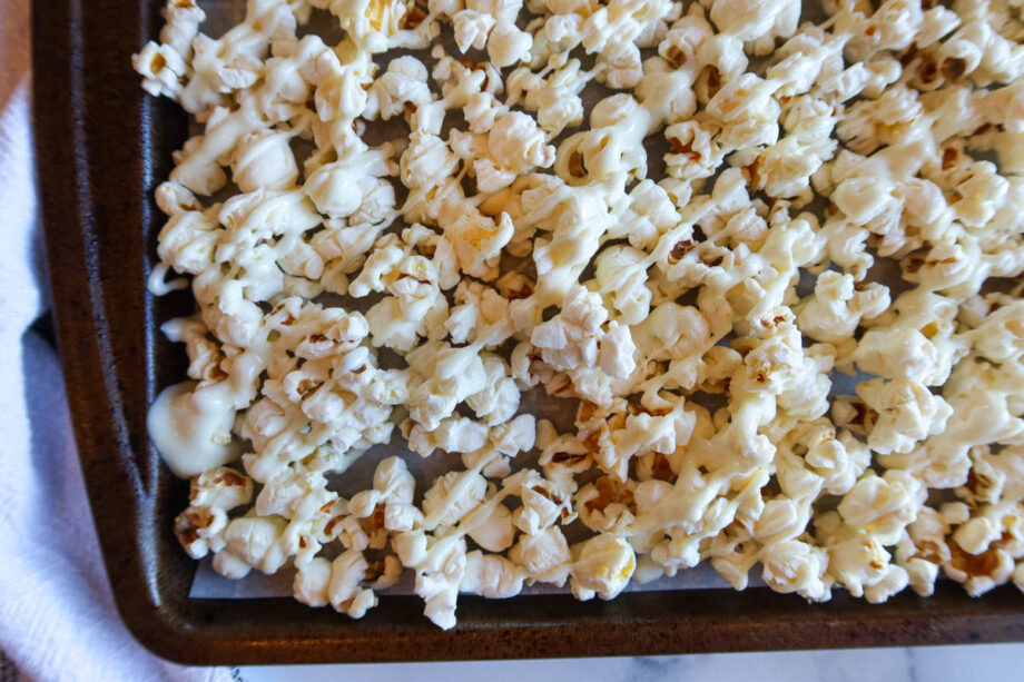 Popcorn on a parchment paper lined baking sheet, drizzled in white chocolate.