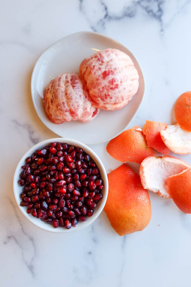 A peeled grapefruit and small bowl of pomegranate seeds on a white countertop.