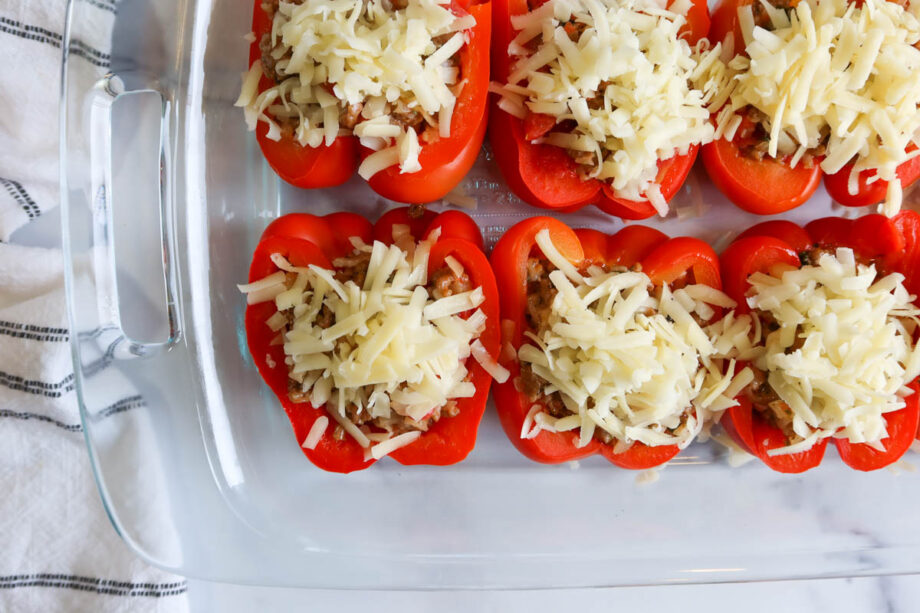 Bell peppers stuffed with filling, sprinkled with cheese and lined in a glass baking dish.