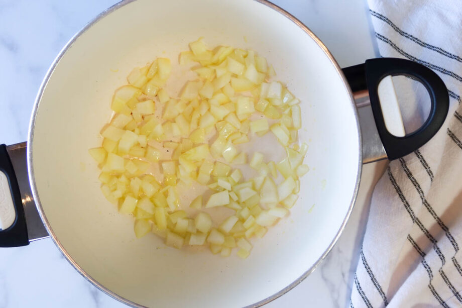 Sautéing diced onion in a large white soup pot with black handles.