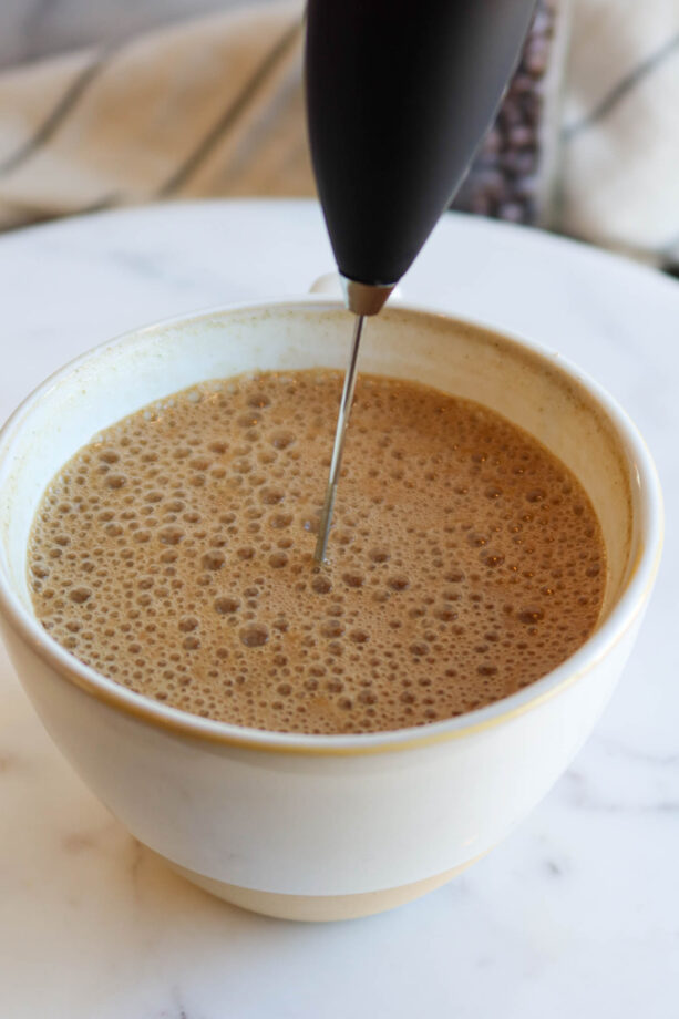 Using a milk frother to mix hot coffee and protein powder together.