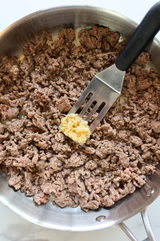 Adding minced garlic to browned ground beef.