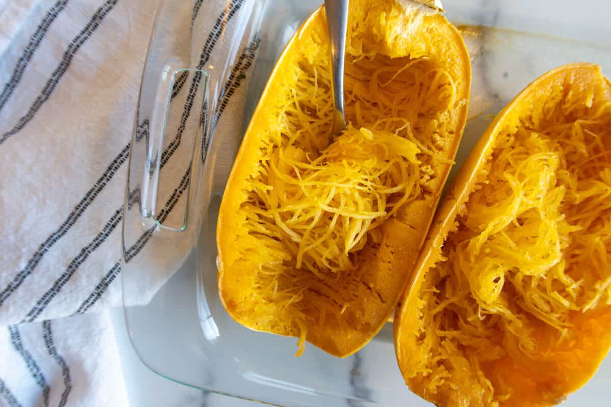 Cooked spaghetti squash with a fork pulling strands from shell.
