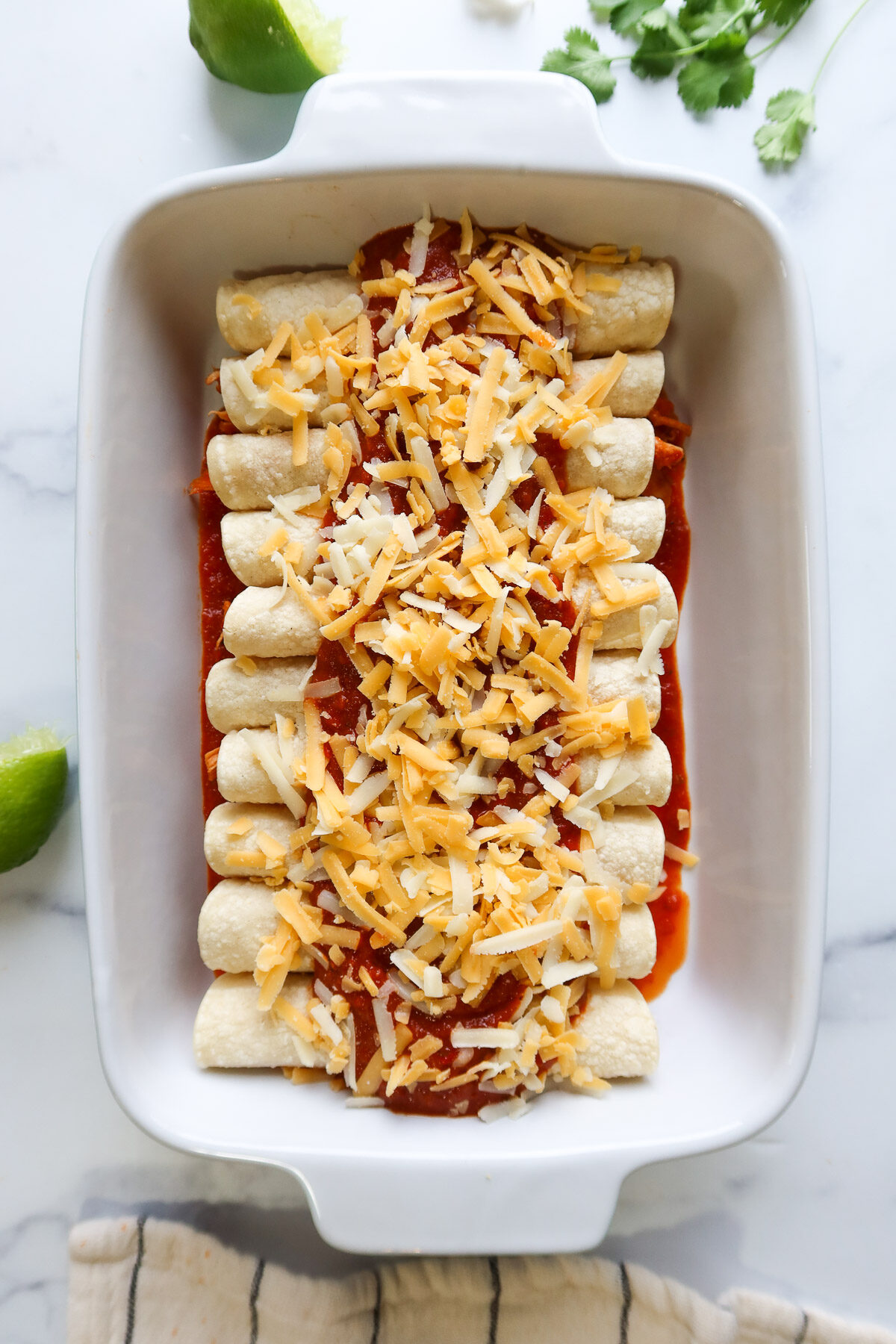 Enchiladas lined in a baking dish and covered with tinga sauce and shredded cheese.