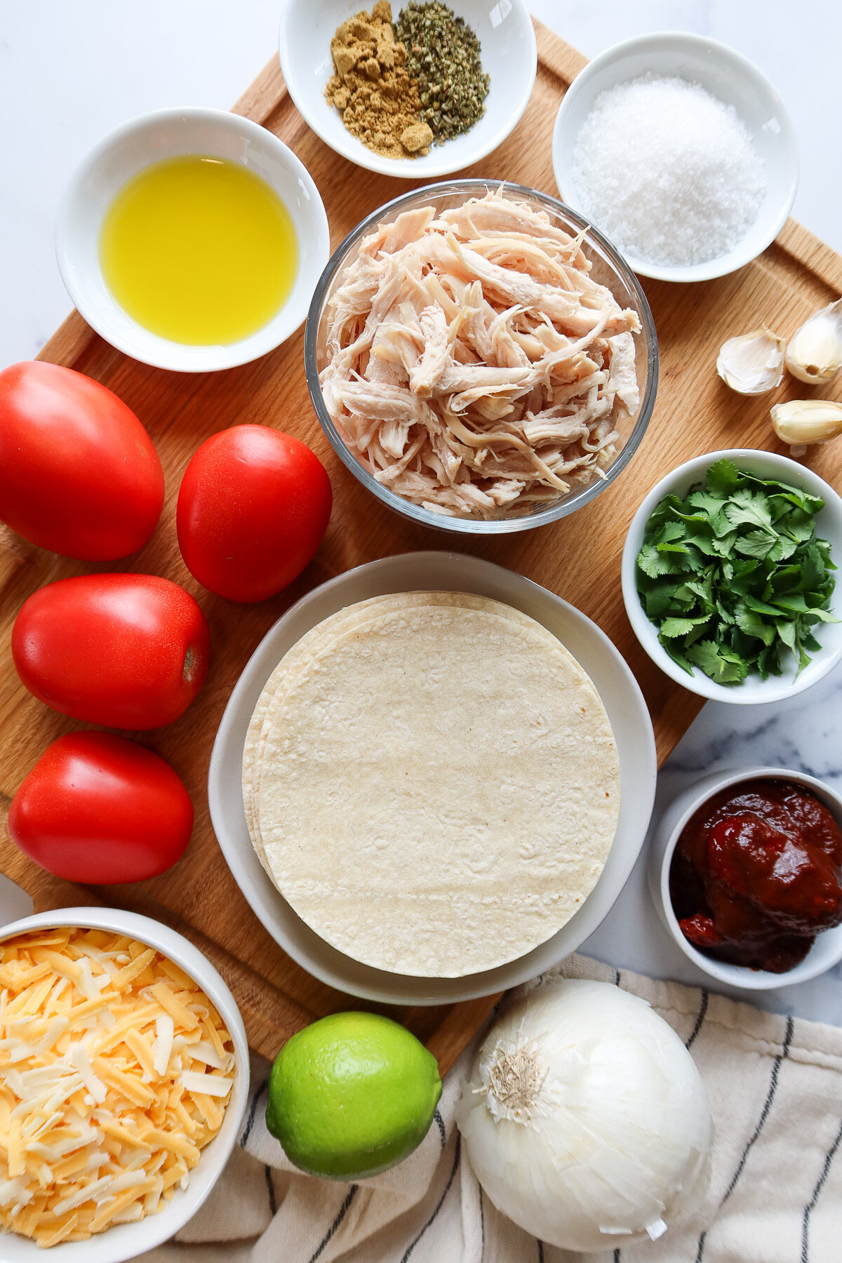 Ingredients for chicken tinga enchiladas arranged on a large, wooden cutting board.