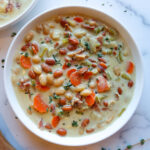 Creamy ham bean soup in a white serving bowl with fresh chopped thyme sprinkled atop.
