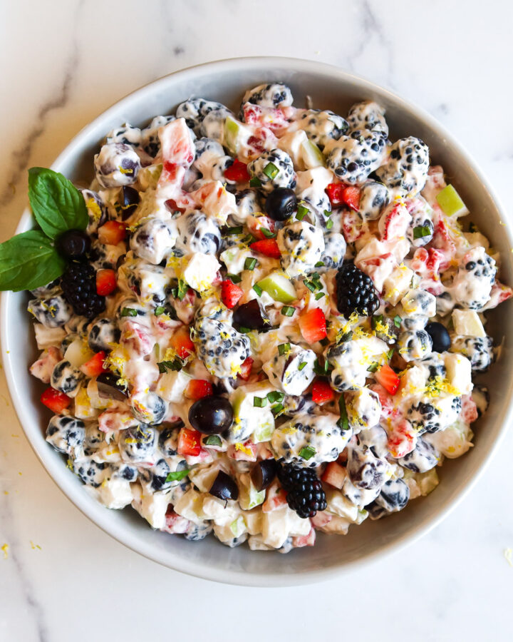 Fruit salad with whipped cream in a white serving bowl.