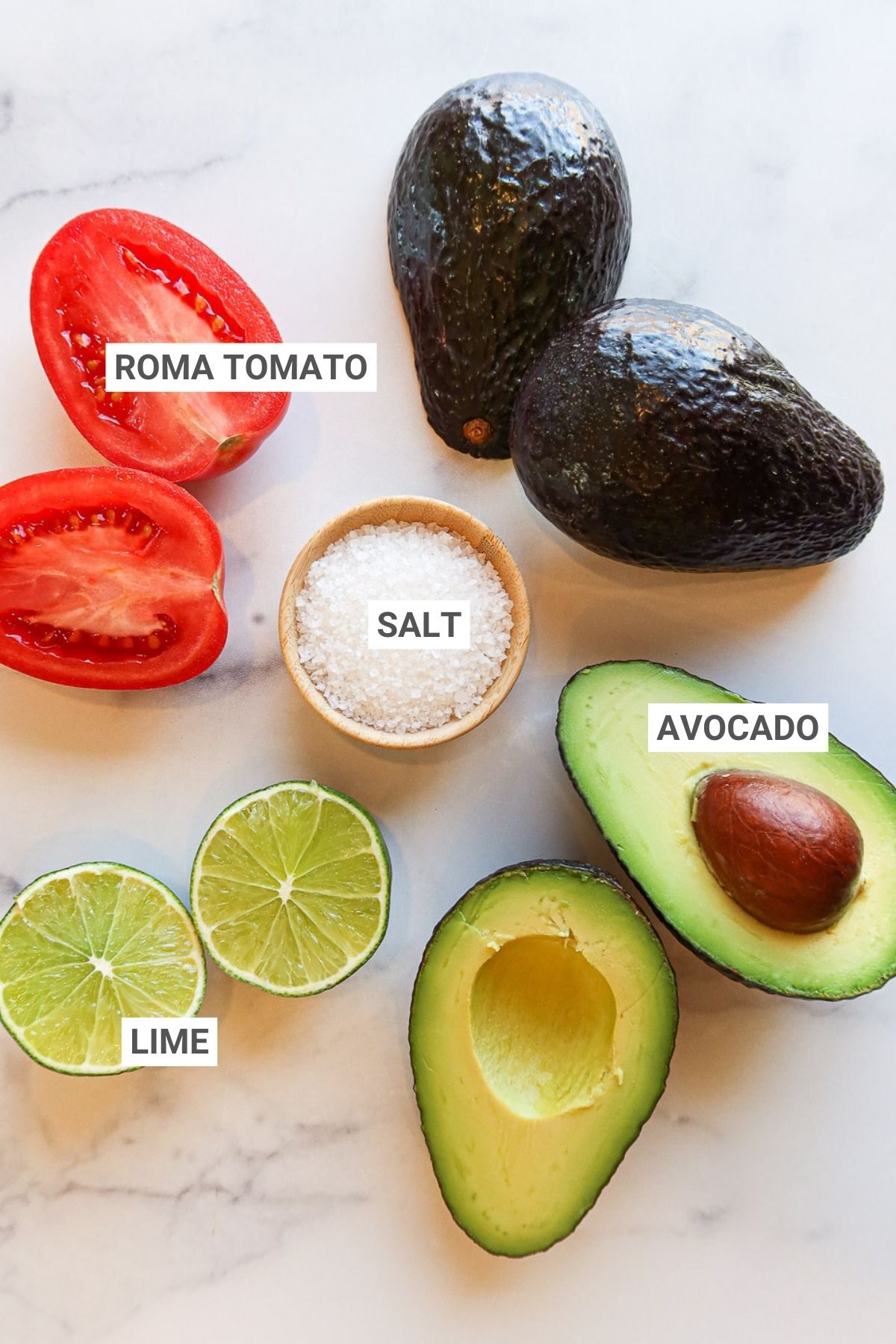 Ingredients for guacamole arranged on a white countertop with text overlay labels. 