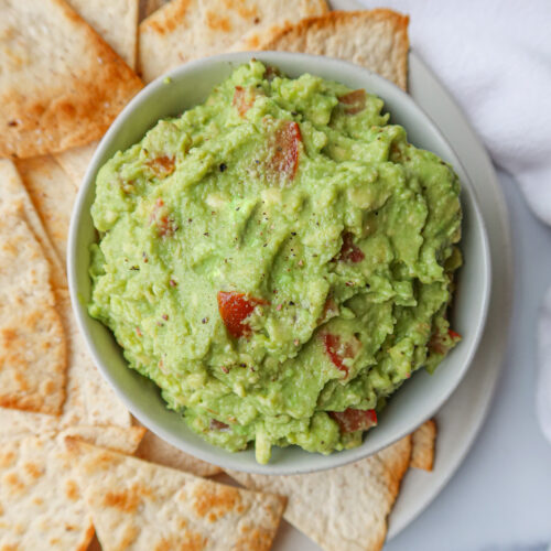 Guacamole in a white serving bowl surrounded by tortilla chips.