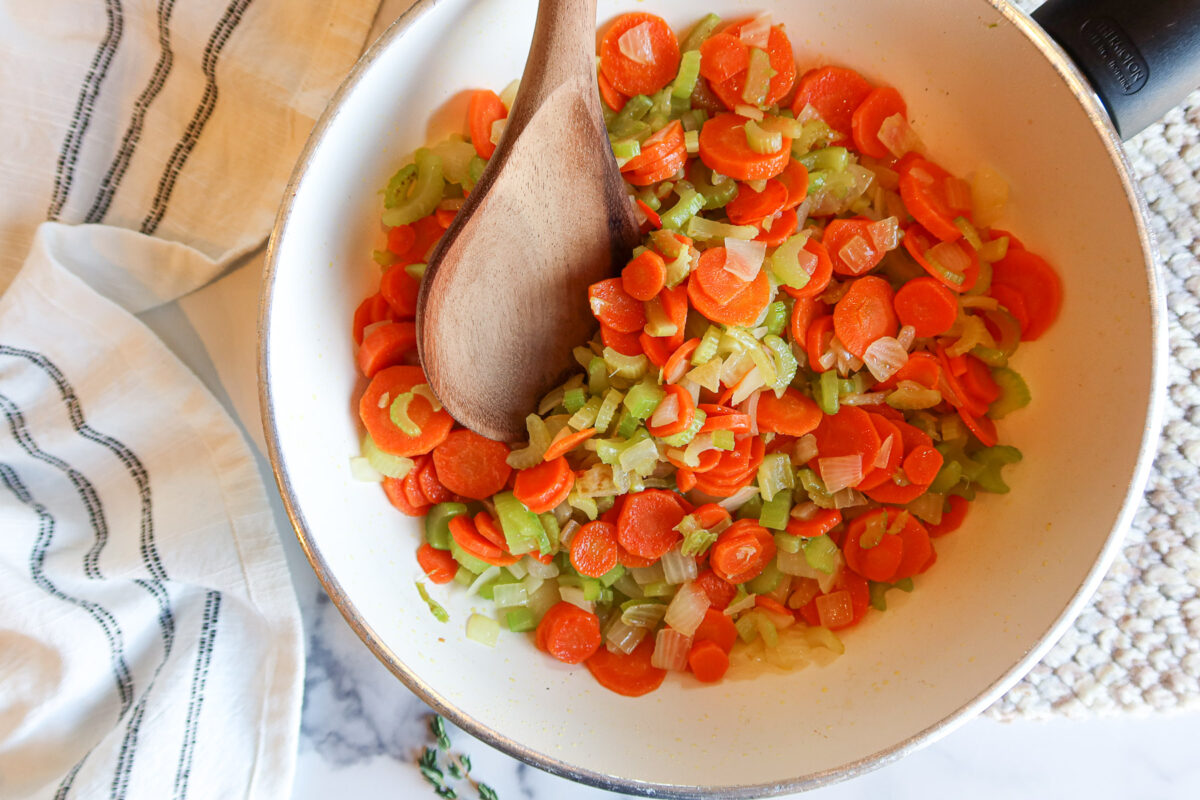 Sautéing carrot, onion and celery in a white frying pan.