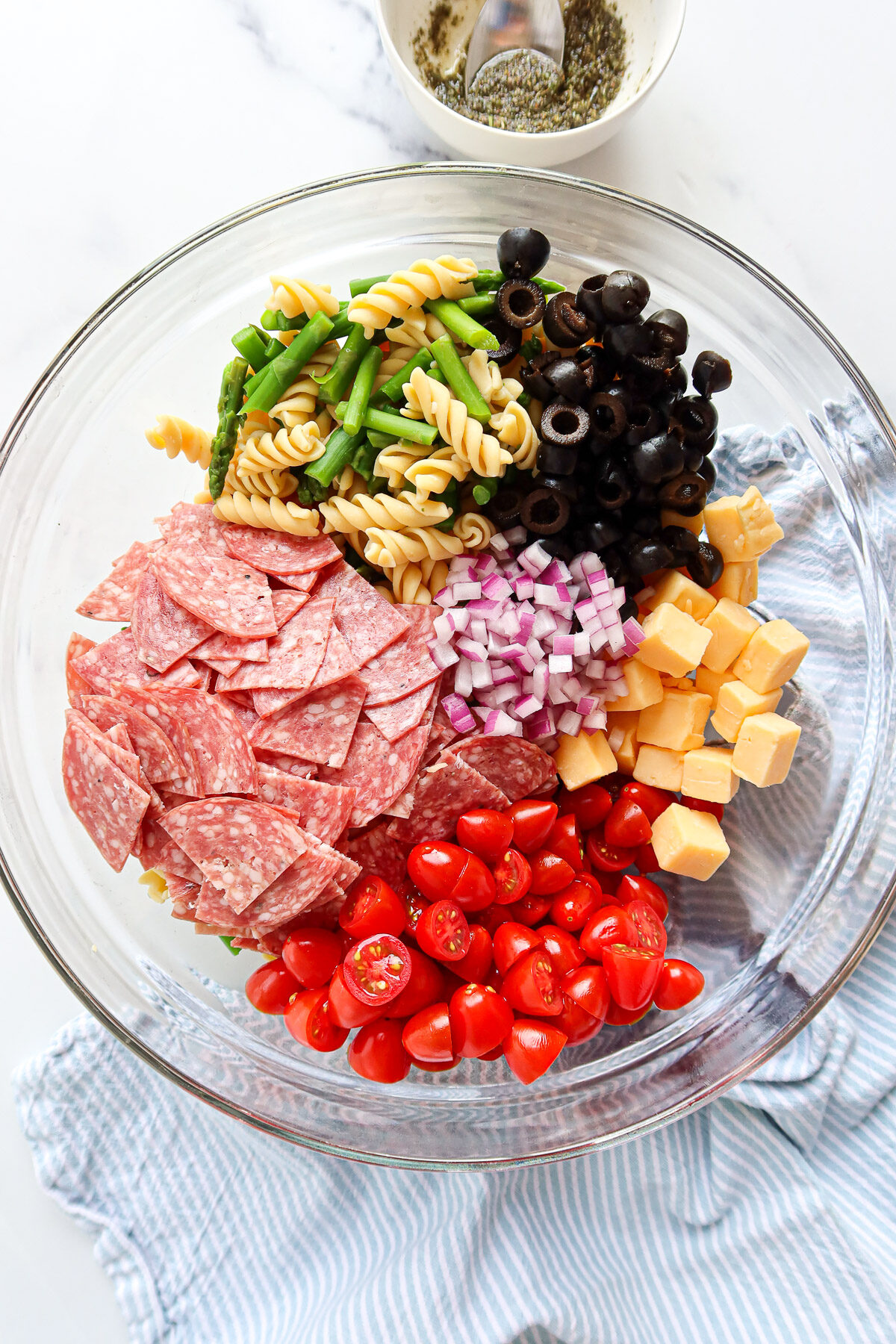 Pasta salad ingredients measured into a large, glass mixing bowl.
