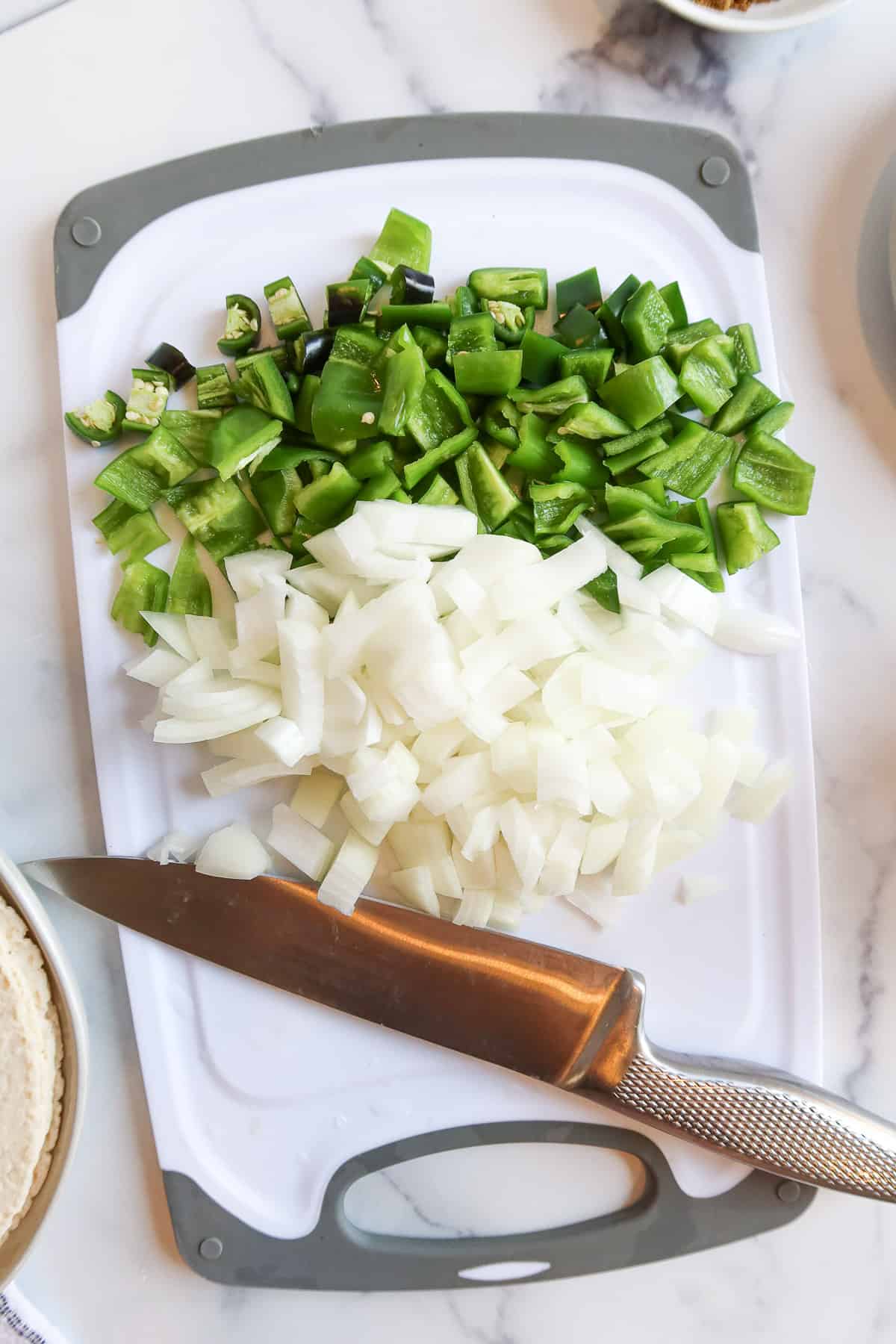 Chopped jalapenos, green bell peppers and white onion on a cutting board.
