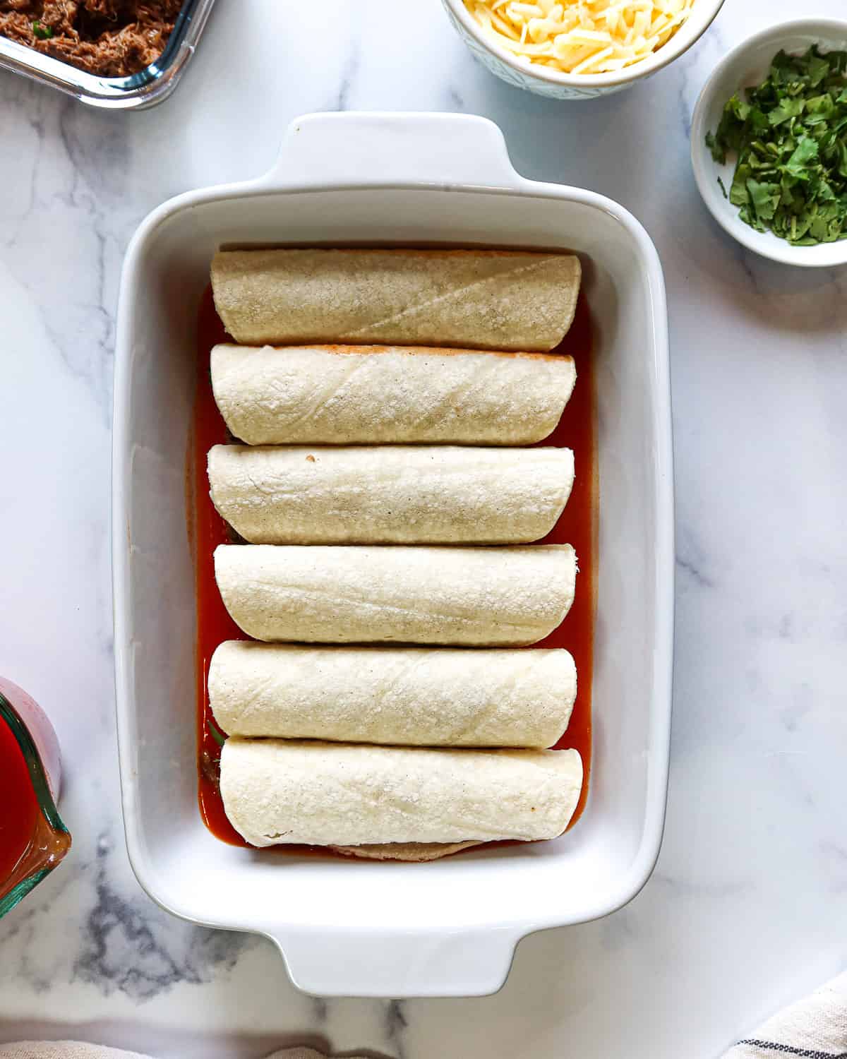 Enchiladas lined in a white baking dish.