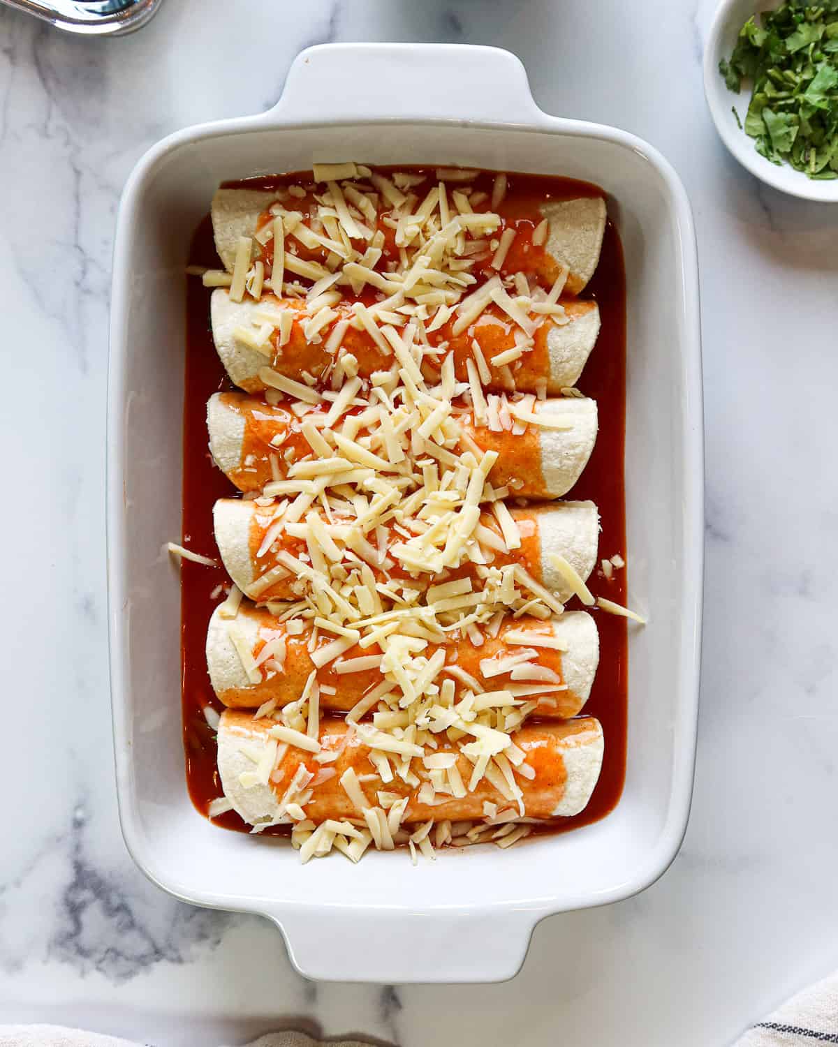 Enchiladas lined in a baking dish and covered in red sauce and shredded cheese.
