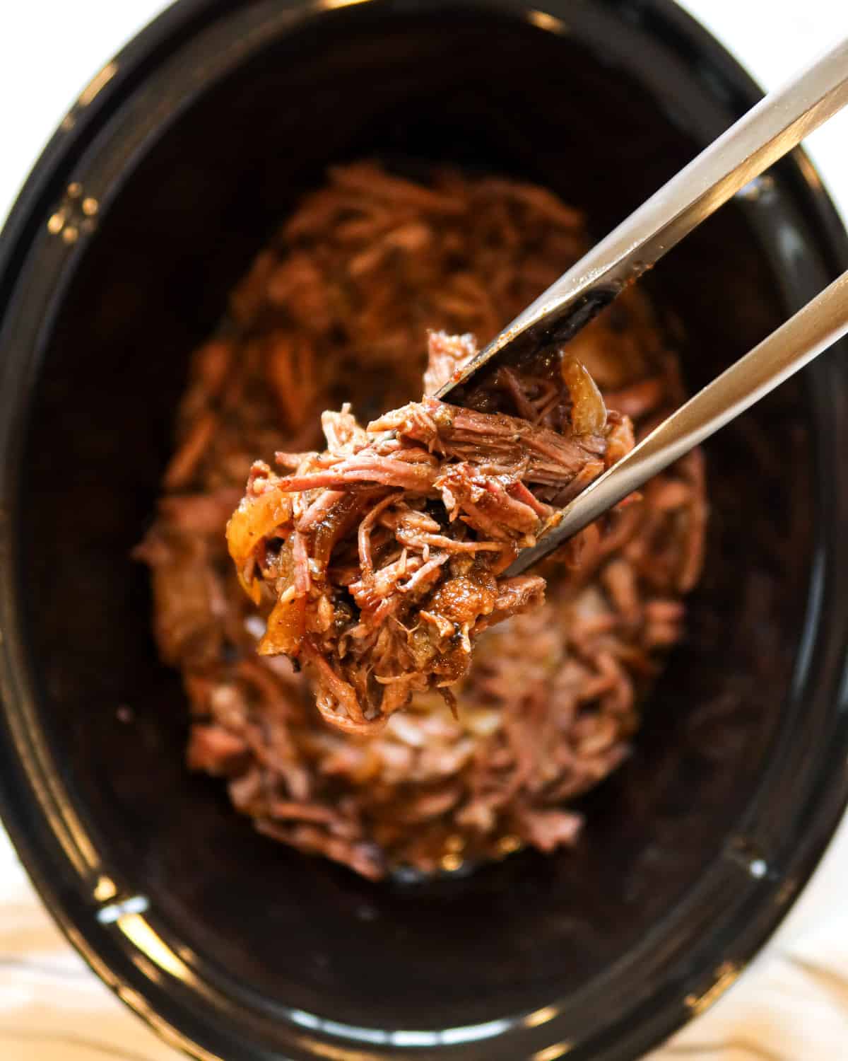 Close up of Mexican shredded beef held in kitchen tongs.