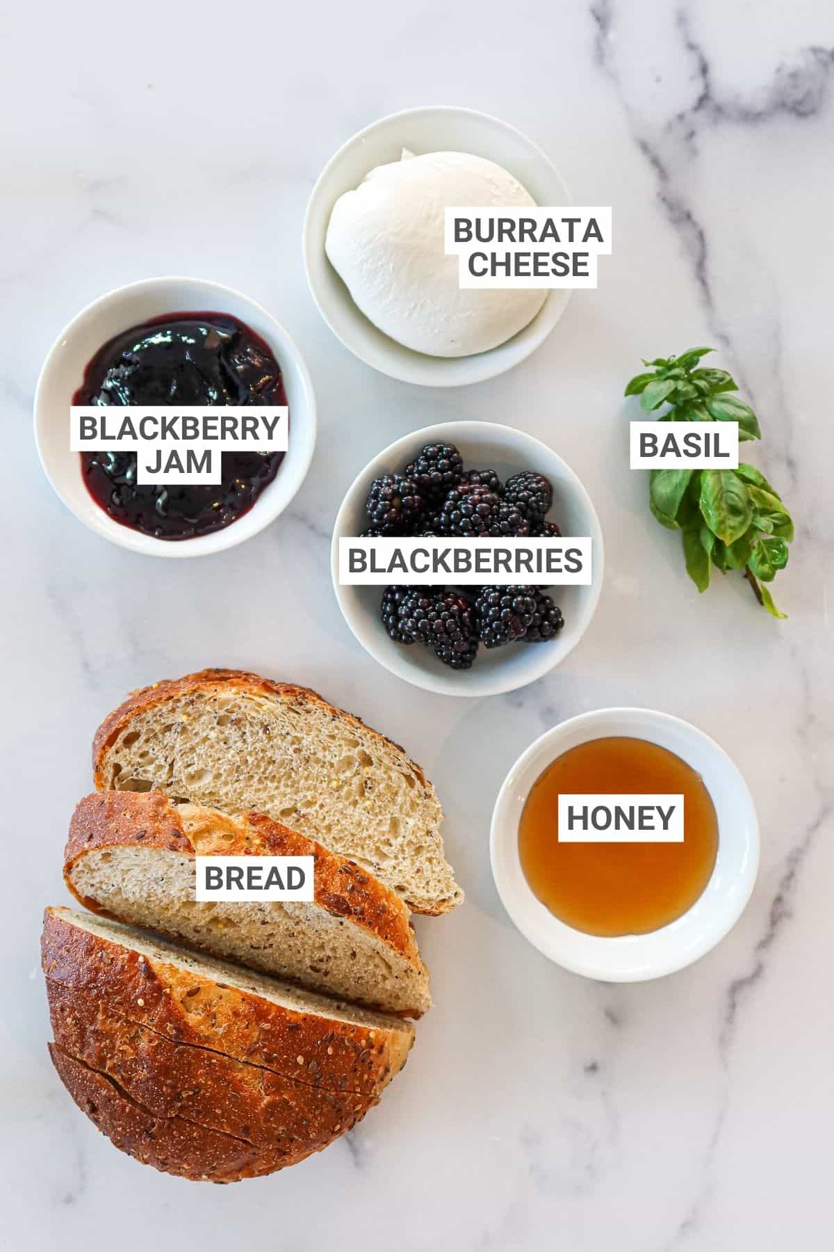Ingredients for blackberry burrata toast on a white countertop with text overlay labels.