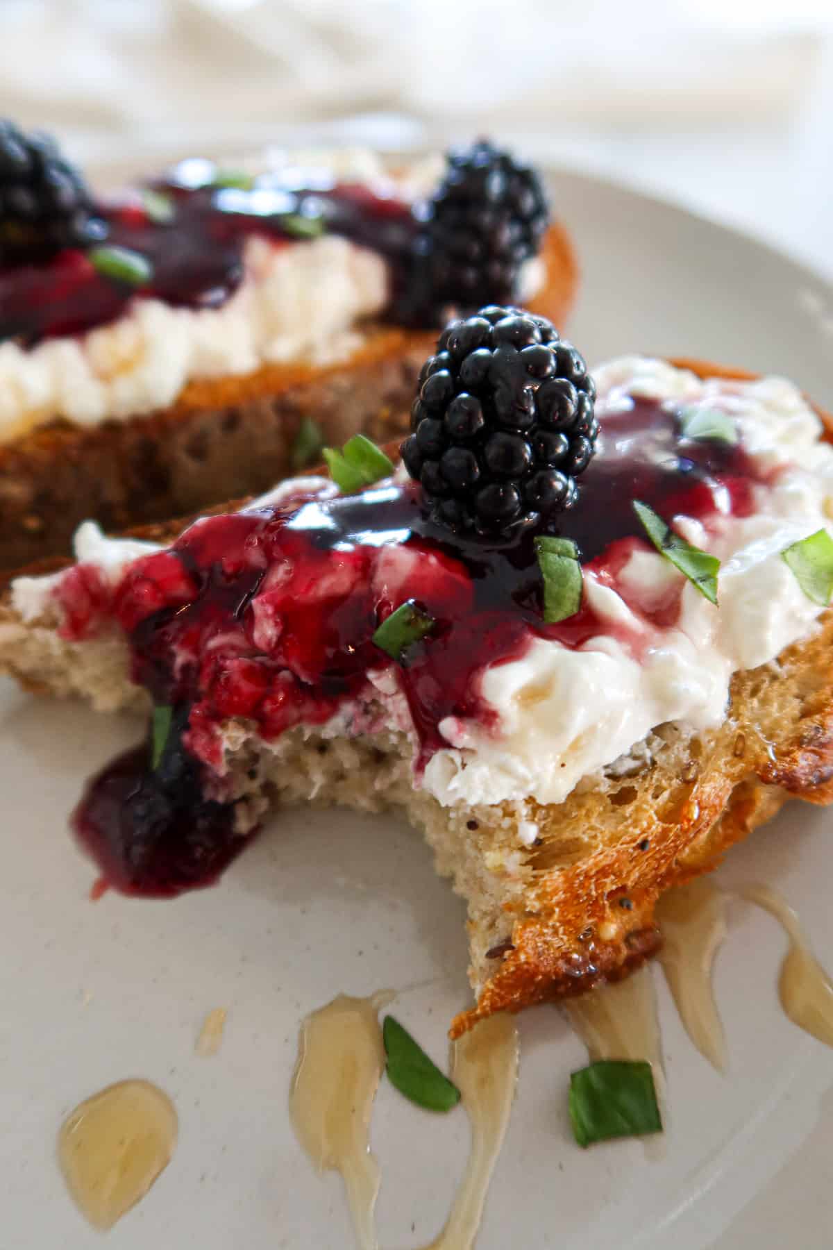 Two slices of blackberry burrata toast. One piece has a bite missing.