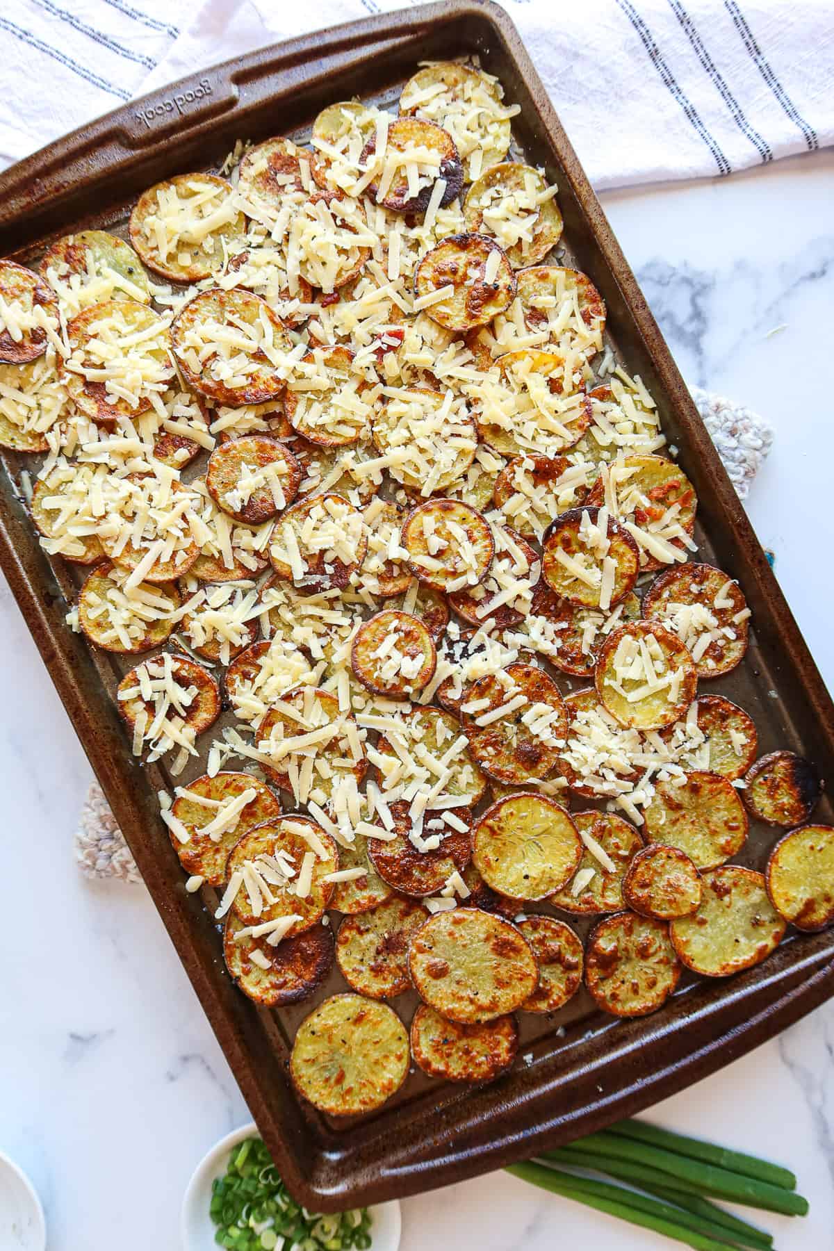 Adding shredded cheese to homemade potato chips atop a baking sheet.