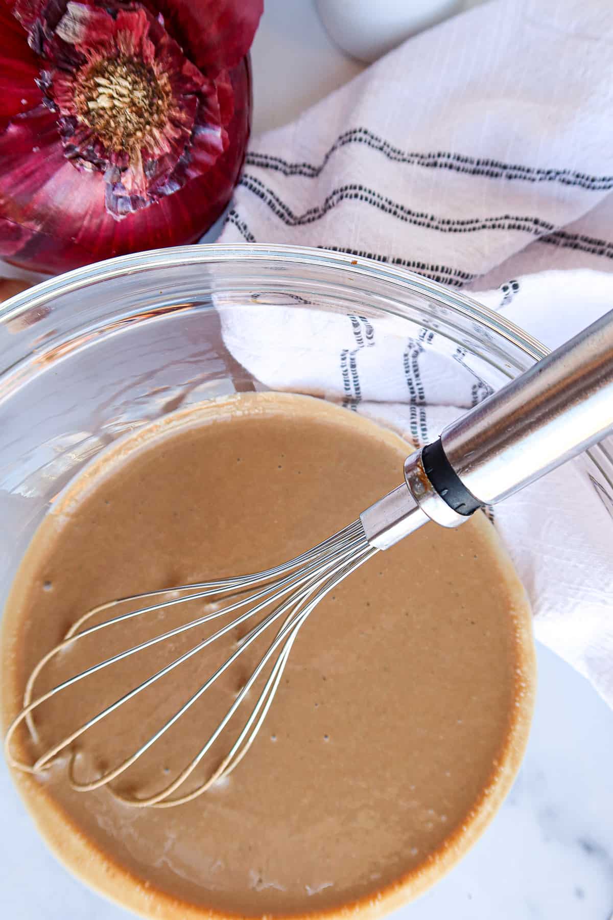 Greek yogurt balsamic dressing in a glass mixing bowl with stainless steel whisk.