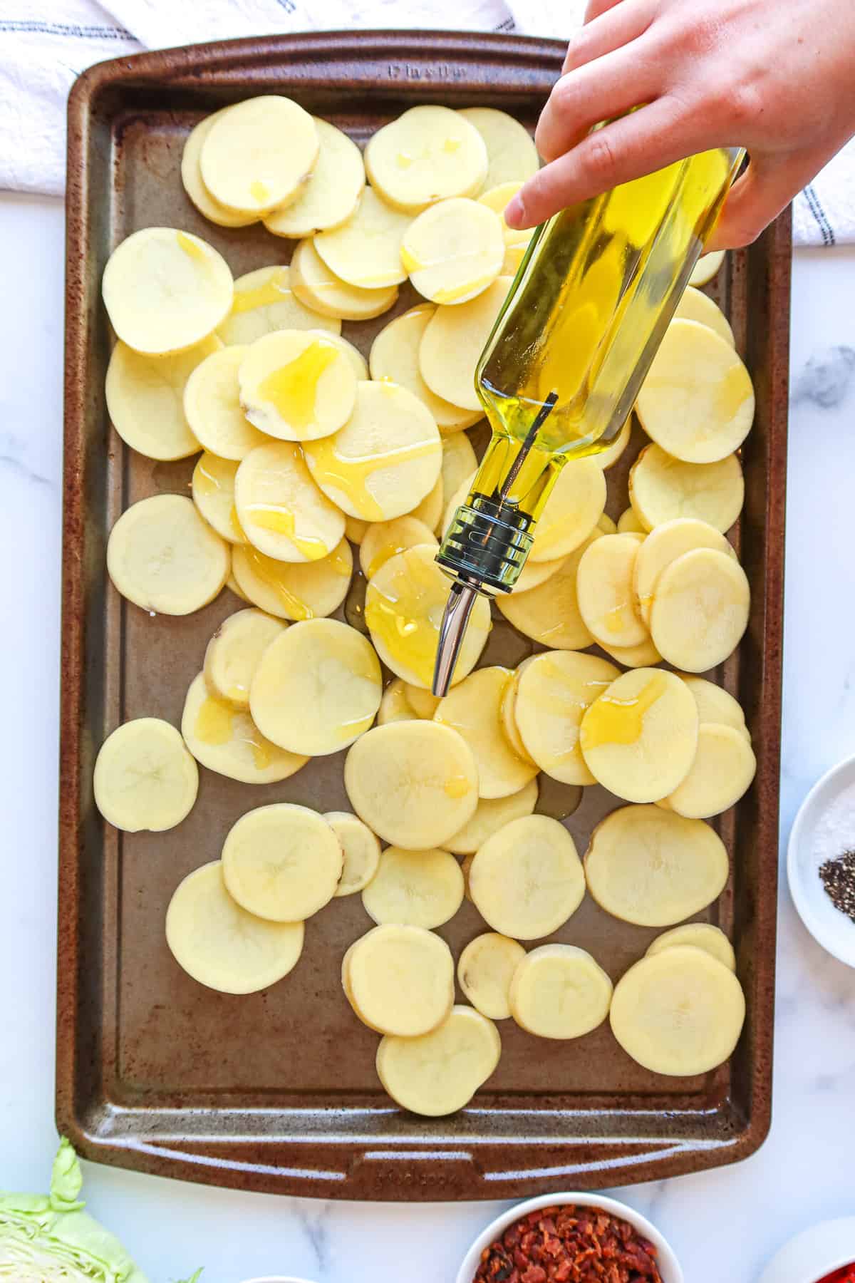 Drizzling olive oil onto thin potato slices atop a baking sheet.