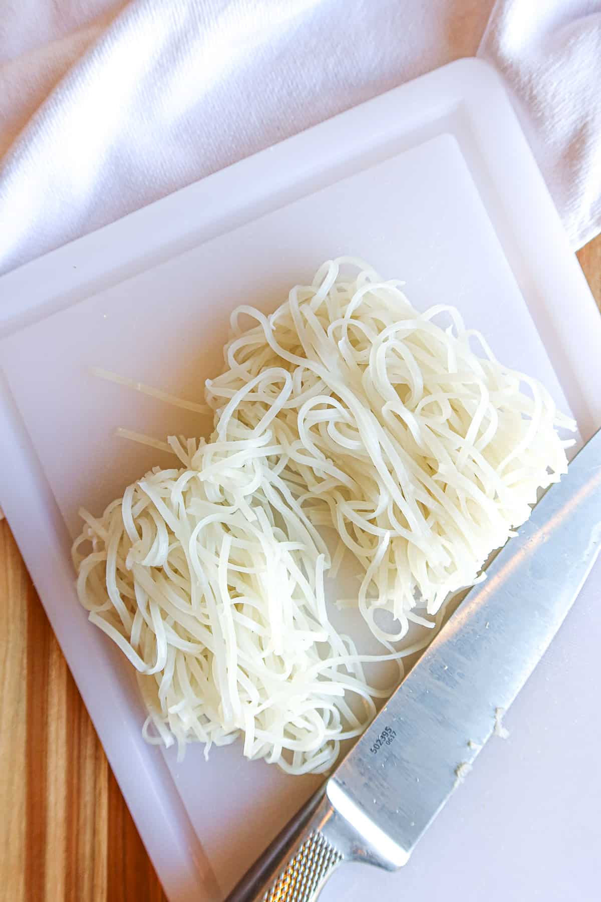 Cooked rice noodles on a white cutting board.