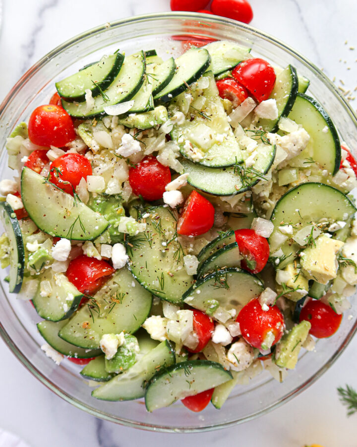 Cucumber, onion and tomato salad in a glass mixing bowl.