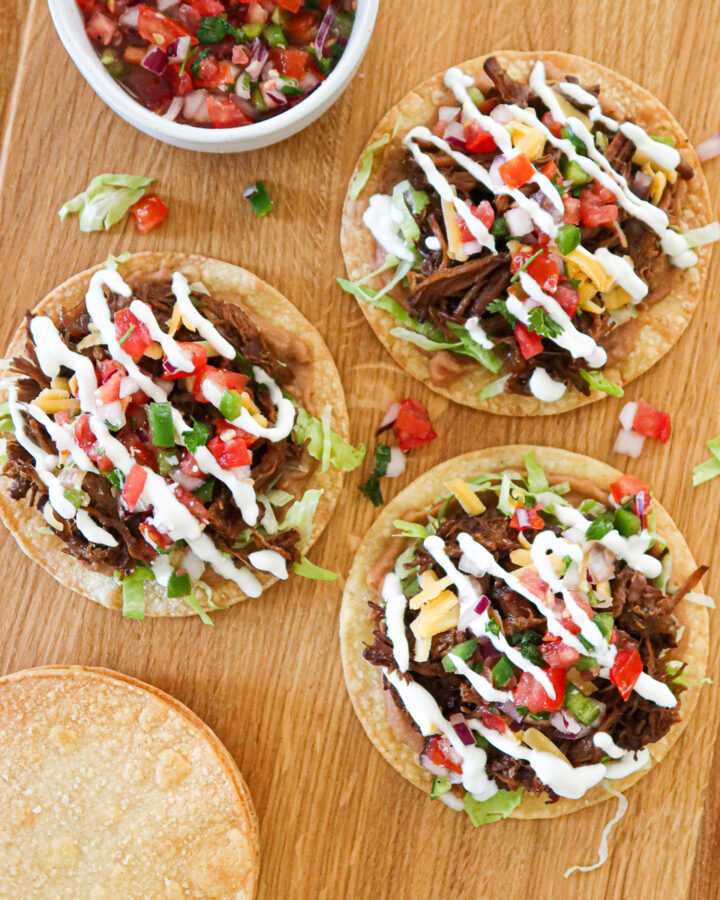 Shredded beef tostadas on a wooden cutting board.