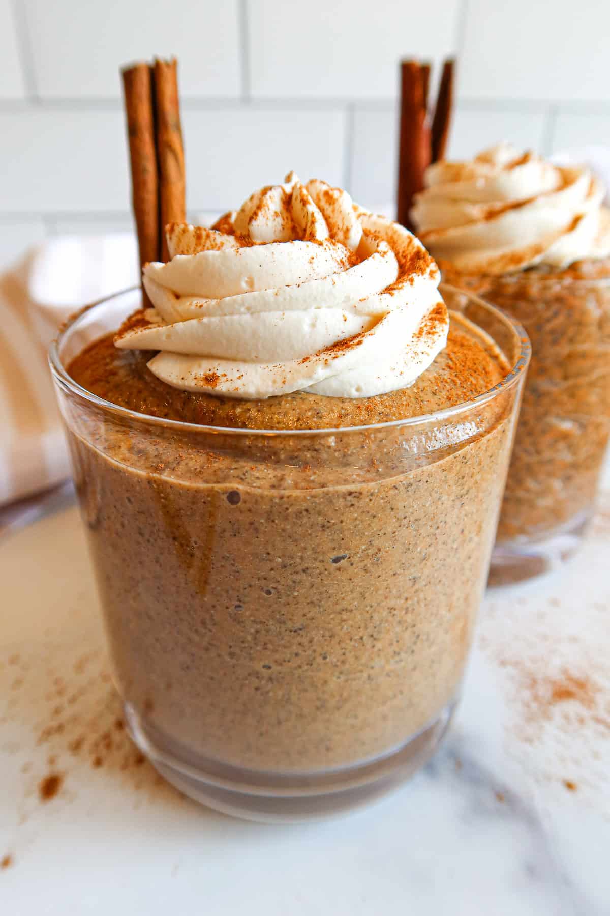 Blended pumpkin chia pudding in a serving glass with whipped topping and cinnamon stick.