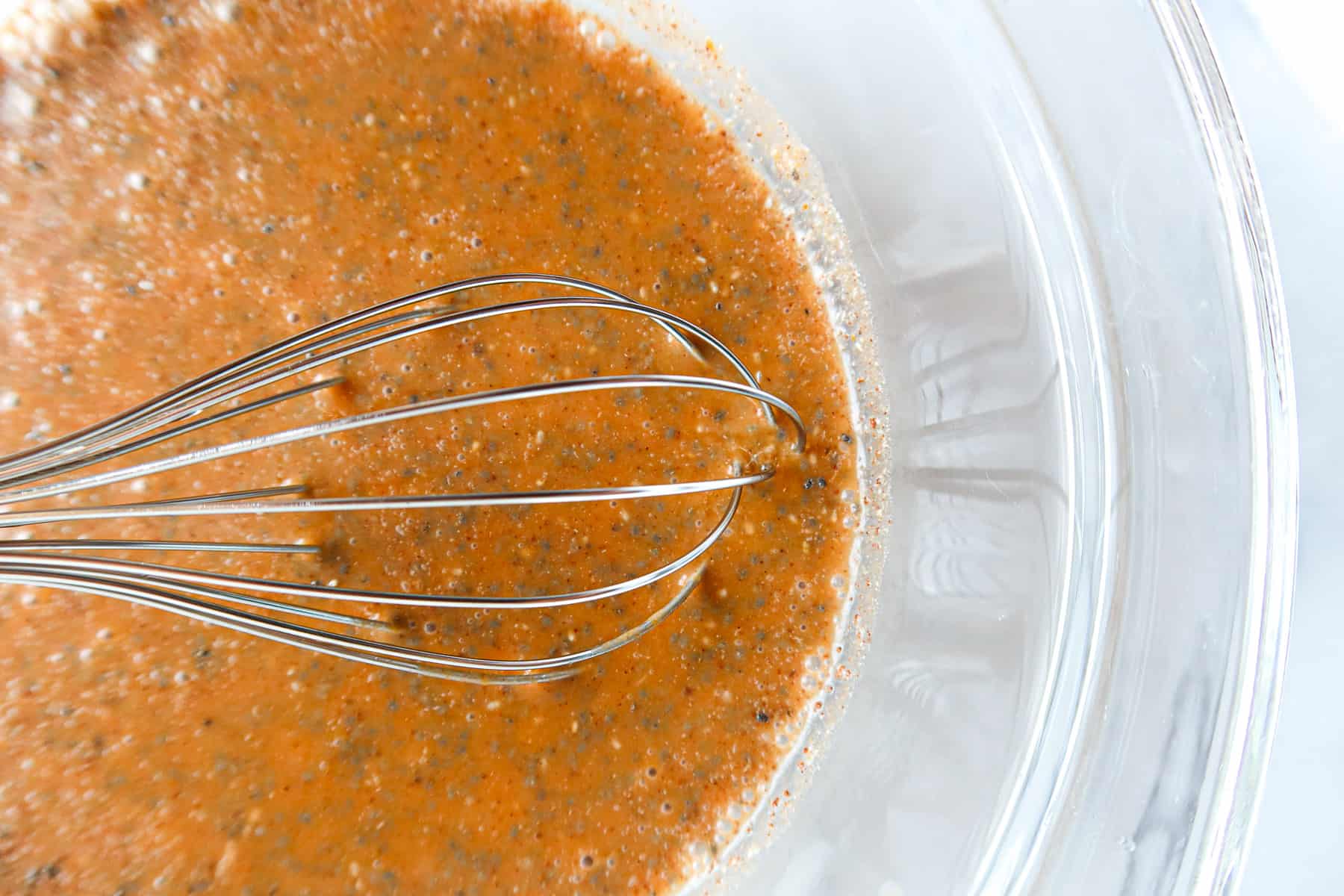 Ingredients for pumpkin chia pudding whisked together in a large, glass bowl.