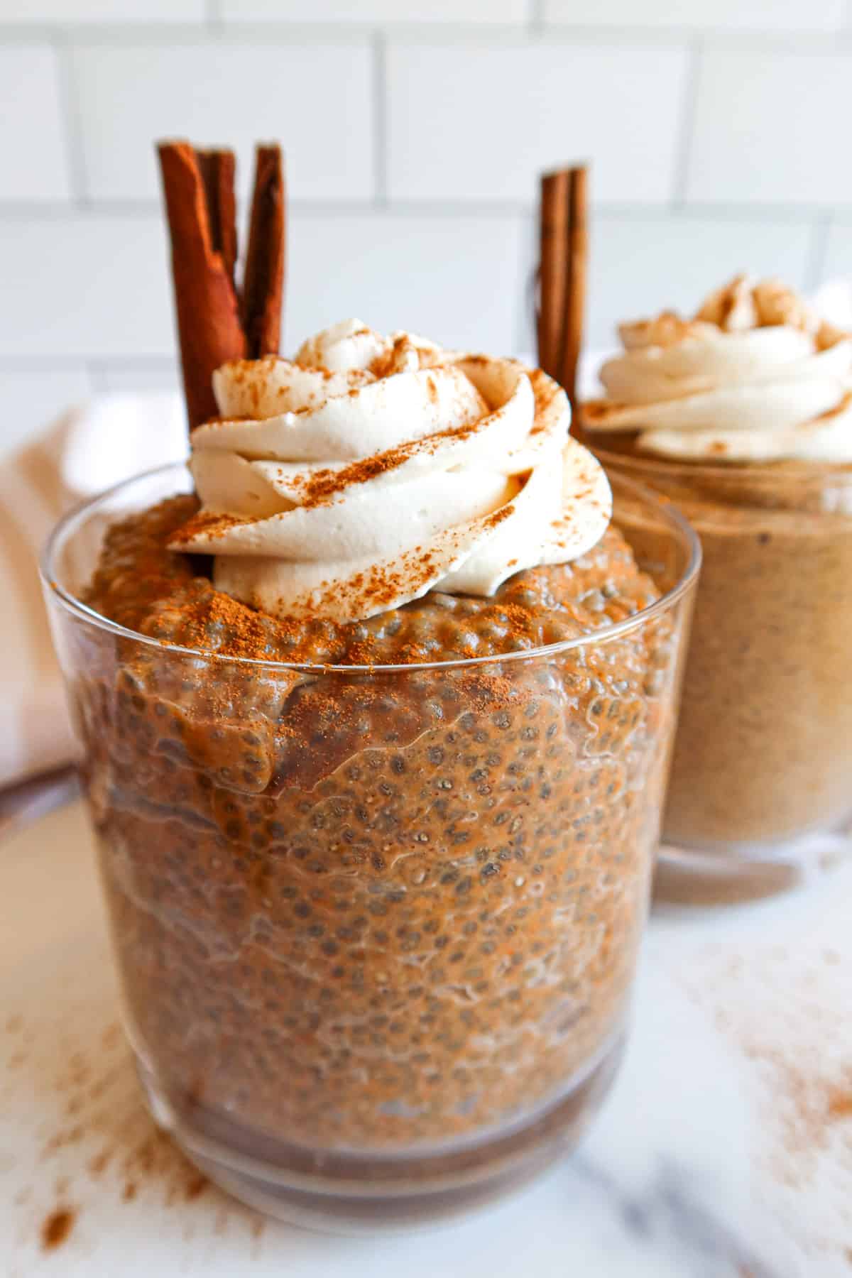 Pumpkin chia pudding in a serving glass with whipped topping and a cinnamon stick.