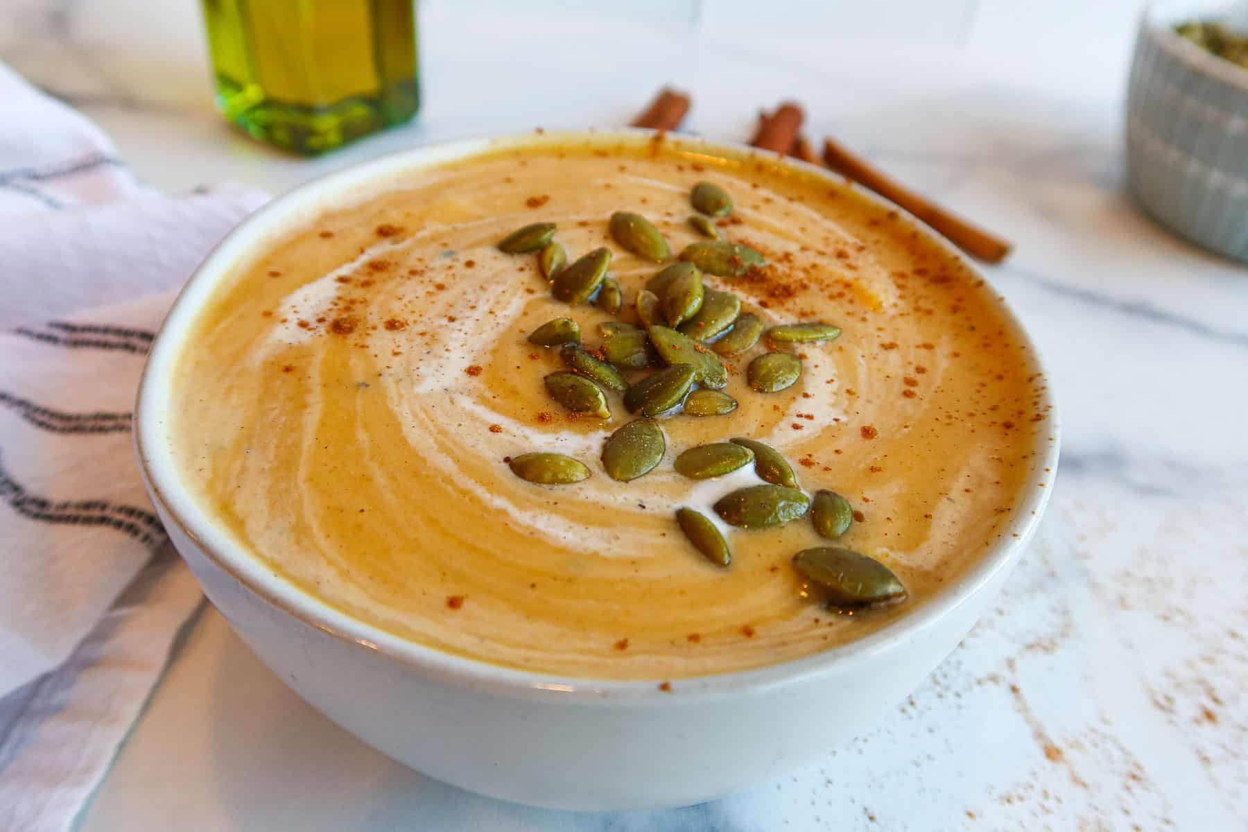 Bowl of butternut squash soup topped with coconut milk, cinnamon and pumpkin seeds.