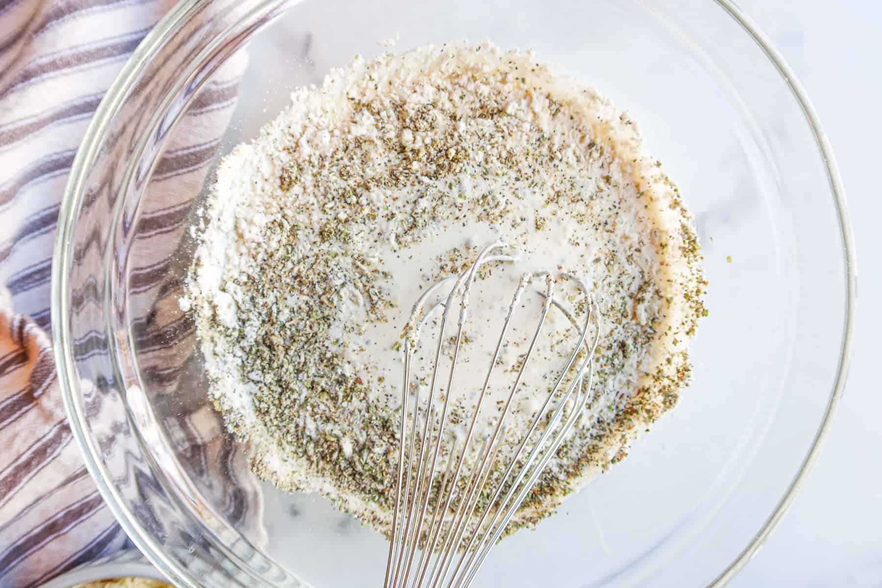 Whisking heavy cream, salt, pepper, marjoram and gluten free flour together in a bowl.