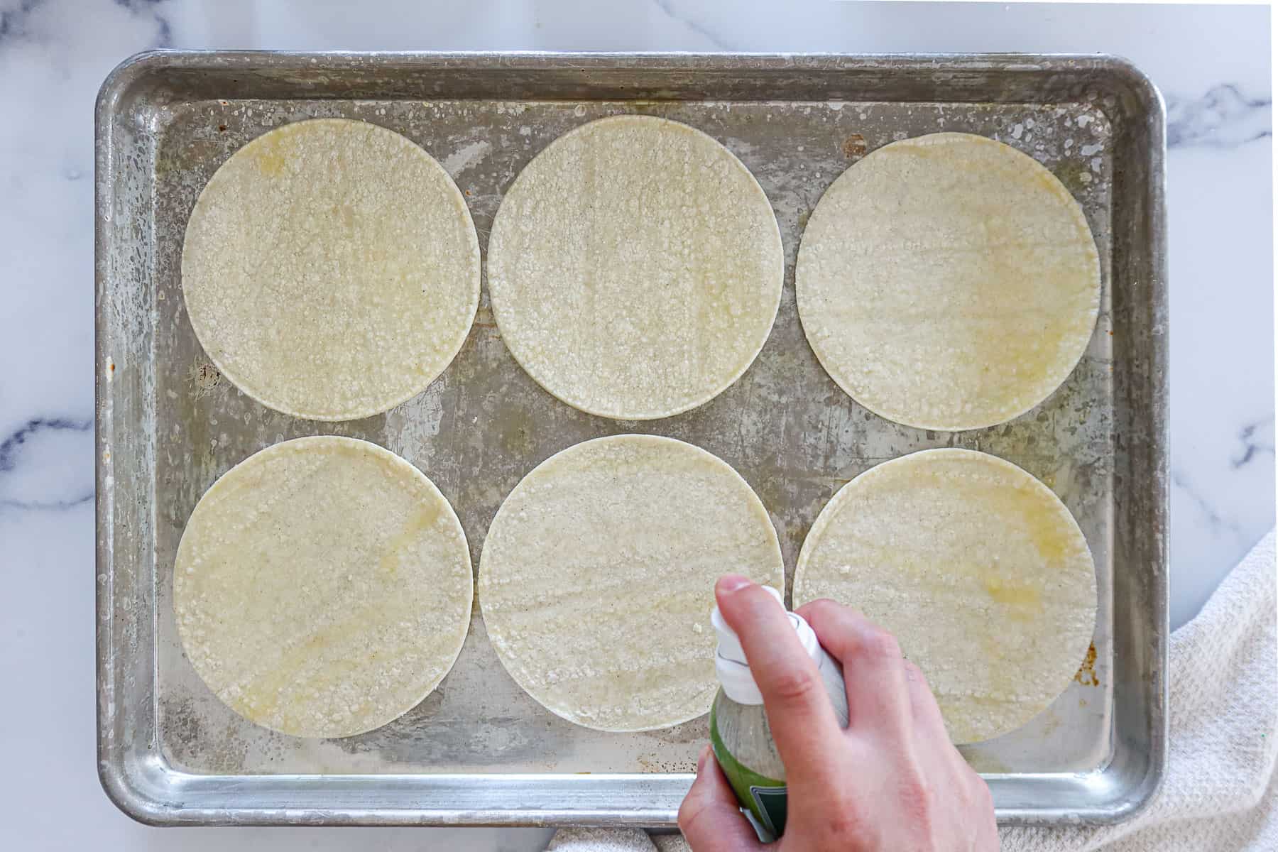 Coating corn tortillas in olive oil cooking spray.