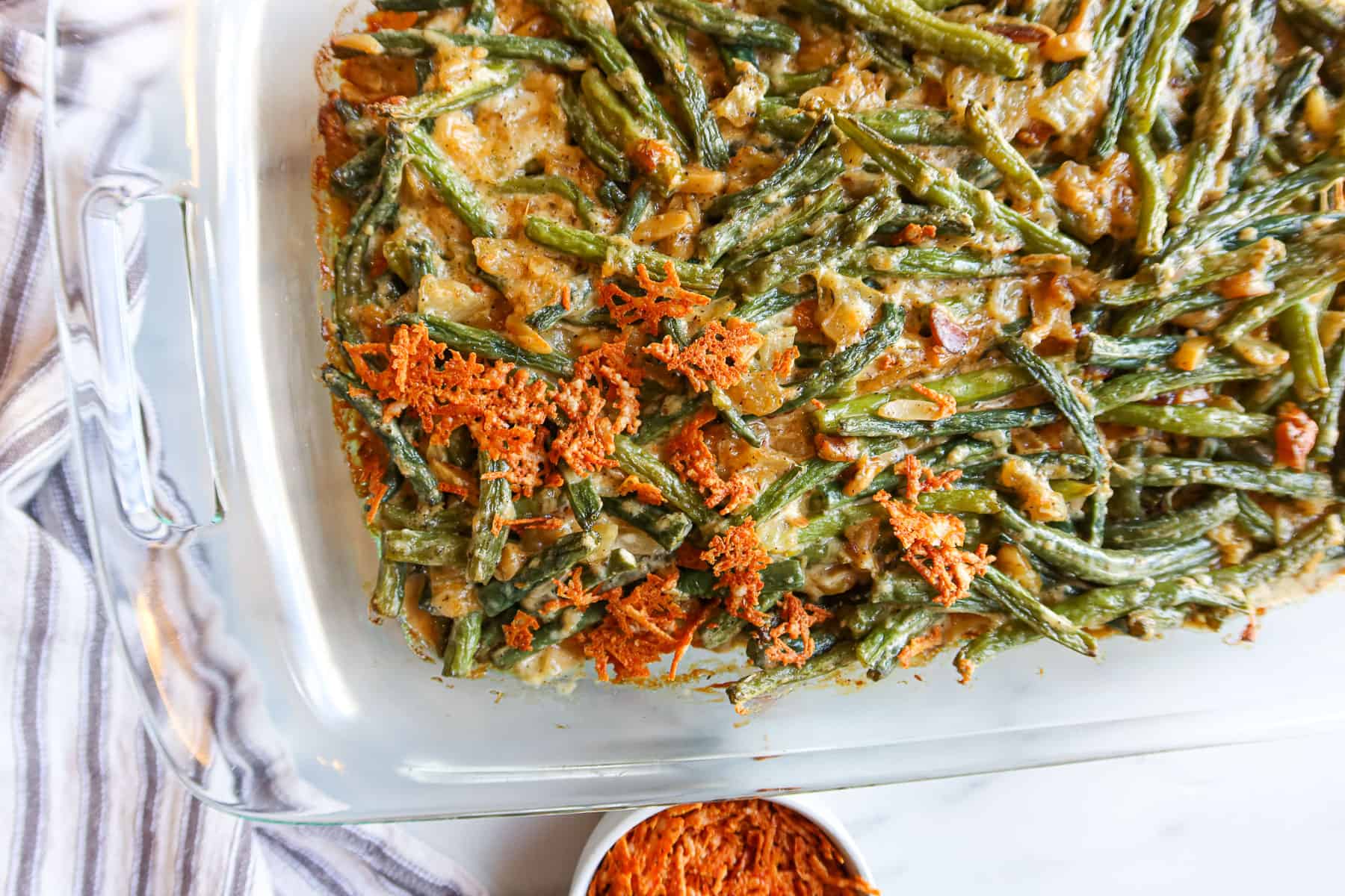 Sprinkling parmesan cheese crisps on green bean casserole in a baking dish.