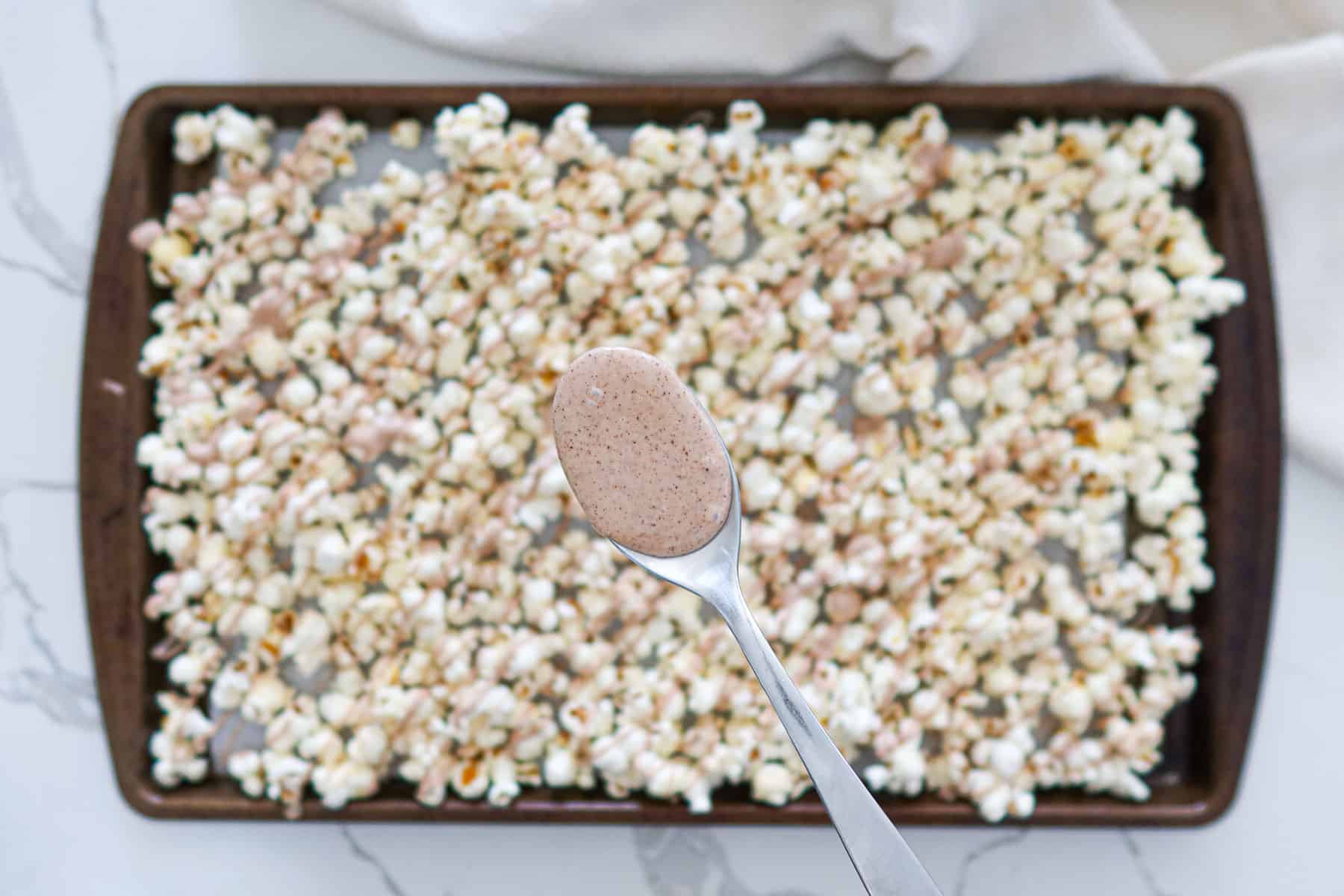 Adding cinnamon spiced melted white chocolate to popcorn.