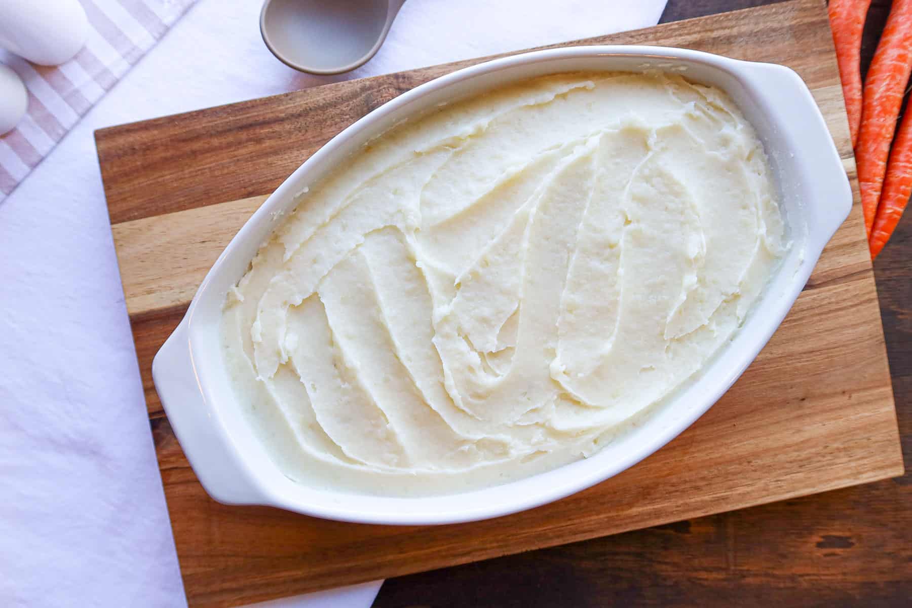 Mashed potatoes spread evenly over filling in white baking dish.