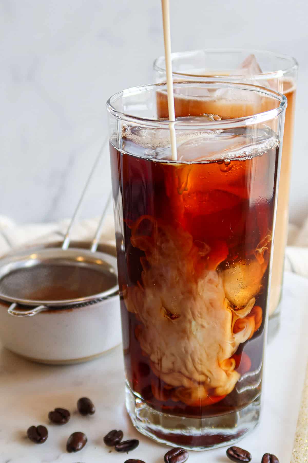 Adding a protein shake to cold brew coffee in a drinking glass.