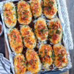 Cheesy twice baked potatoes on a foil lined baking sheet.